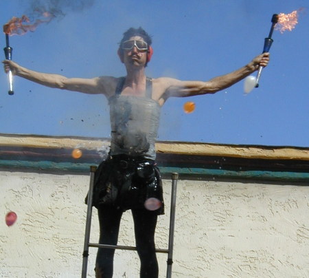 Dexter Tripp balancing on a ladder while firecrackers duct-taped to him explode and people throw water balloons at him
