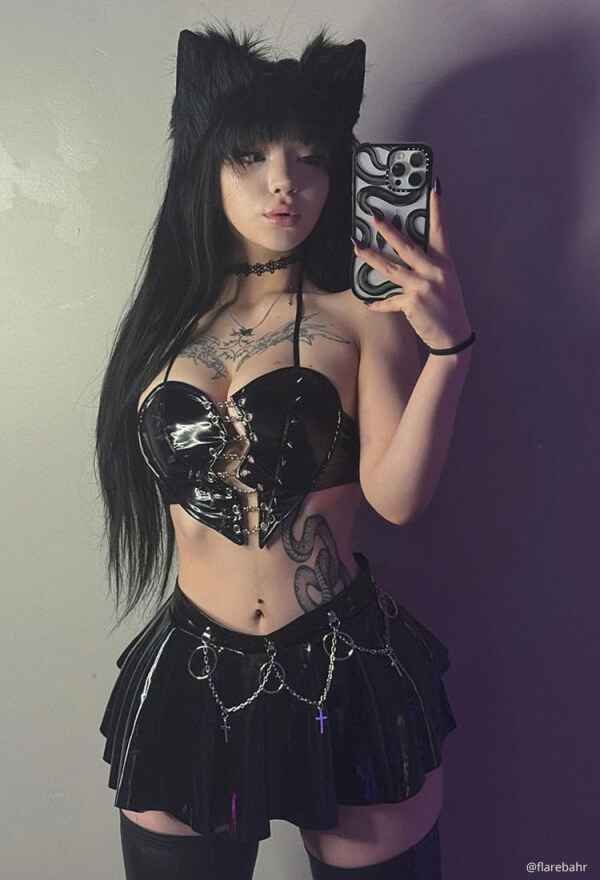 A cute woman in a black PVC outfit takes a selfie.